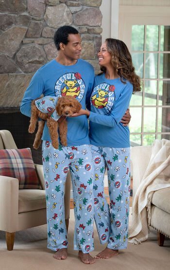 Woman and Man in front of the fireplace holding their dog, all wearing matching Grateful Dead Pajamas