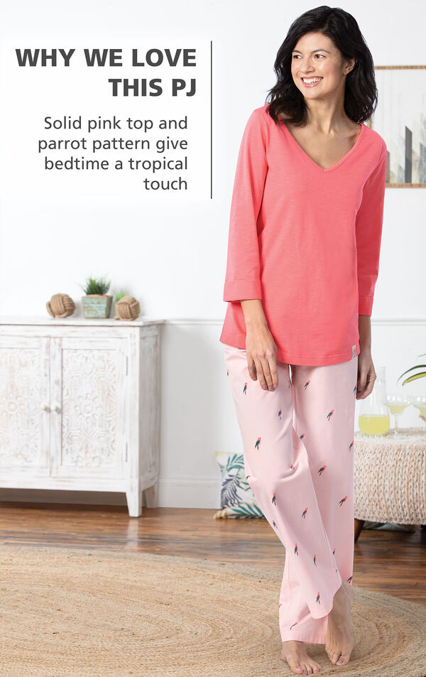 Model by bed wearing Margaritaville Tropical Dreams Pajamas - Pink with the following copy: Solid pink top and parrot pattern give bedtime a tropical touch image number 3