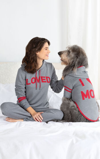 Woman and dog sitting on Bed wearing matching Gray hoodie Pajamas - Woman's says "Loved" on the hoodie and dog's says "I Heart Mom"