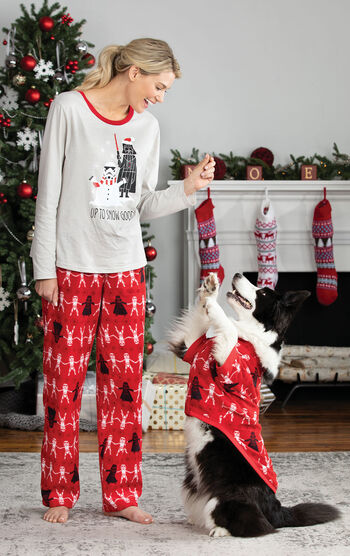Woman standing in front of fireplace wearing Red Star Wars PJs, playing with dog who is wearing Matching Red Star Wars PJs.