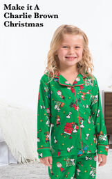 Toddler wearing Charlie Brown Christmas Pajamas by bed with the following copy: Make it a Charlie Brown Christmas. image number 1
