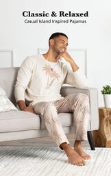 Model sitting on couch wearing Tan Margaritaville Easy Island Men's Pajamas with the following copy: Classic and Relaxed - Casual Island Inspired Pajamas image number 2