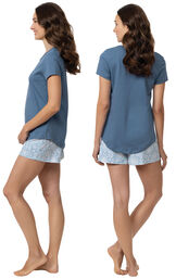 Model wearing blue short sleeve shirt with "let me sleep" text and matching blue and white paisley print shorts, facing away from the camera and then facing to the side image number 1