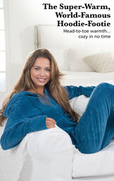 Model sitting on a couch wearing Hoodie-Footie - Blue with the following copy: The Super-Warm, World-Famous Hoodie-Footie. Head to toe warmth, cozy in no time. image number 2