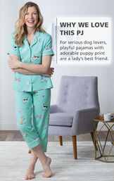 Model standing by chair wearing Light Blue Dog Print Short Sleeve Button-Front Capri PJ for Women with the following copy: For serious dog lovers, playful pajamas with adorable puppy print are a lady's best friend image number 2