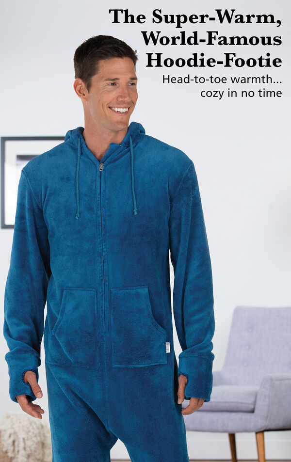 Model wearing Hoodie Footie™ for Men - Blue by chair with the following copy: The Super-Warm, World-Famous Hoodie-Footie - Head-to-toe warmth, cozy in no time image number 1