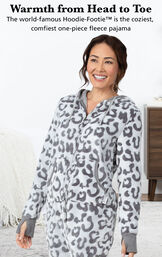 Model wearing Hoodie-Footie - Snow Leopard by bed with the following copy: Warmth from Head to Toe, The world famous Hoodie-Footie is the coziest, comfiest one-piece fleece pajama image number 2