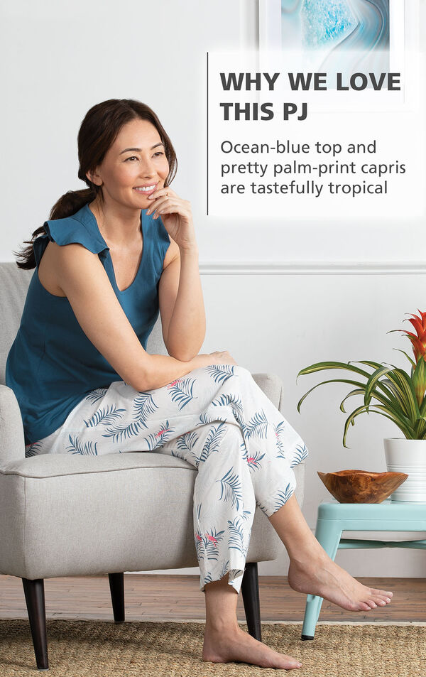 Model wearing Margaritaville Easy Island Capris Pajamas - Blue/White sitting on chair, with the following copy: Ocean-blue top and pretty palm-print capris are tastefully tropical image number 3