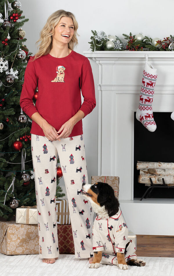 Woman standing in front of fireplace wearing Red and White Holiday Dog Print PJs, playing with dog who is wearing matching pajamas