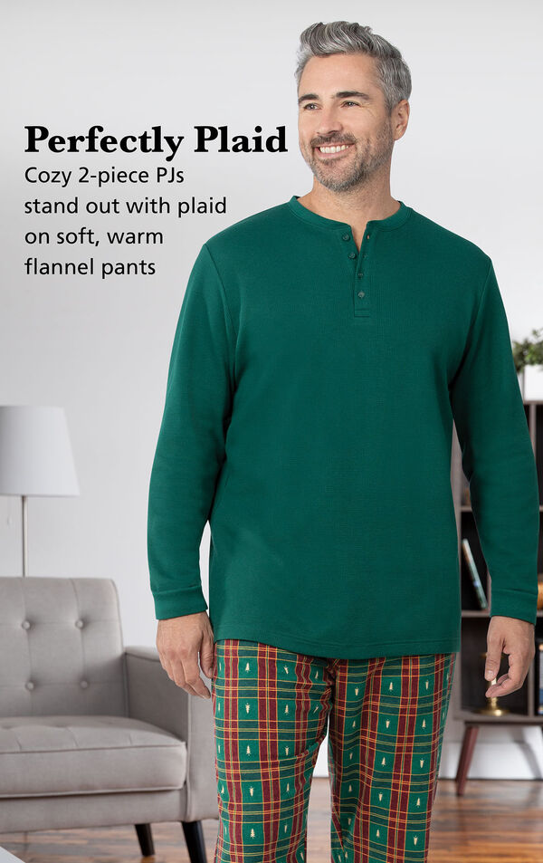 Model wearing Christmas Tree Plaid Men's Pajamas by couch with the following copy: Cozy 2-piece PJs stand out with plaid on soft, warm flannel pants image number 2