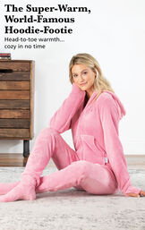 Model sitting on a bed wearing a Pink Hoodie-Footie with the following copy: The Super-Warm, World-Famous Hoodie-Footie. Head-to-toe warmth, cozy in no time. image number 2