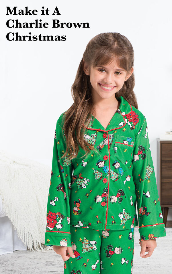 Girl wearing Charlie Brown Christmas Pajamas by bed with the following copy: Make it a Charlie Brown Christmas.
