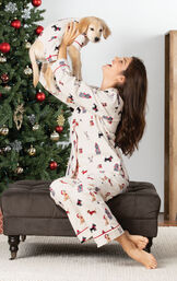 Woman wearing Christmas Dog Print Flannel Pajamas, holding up a puppy wearing matching pajamas by Christmas Tree image number 2