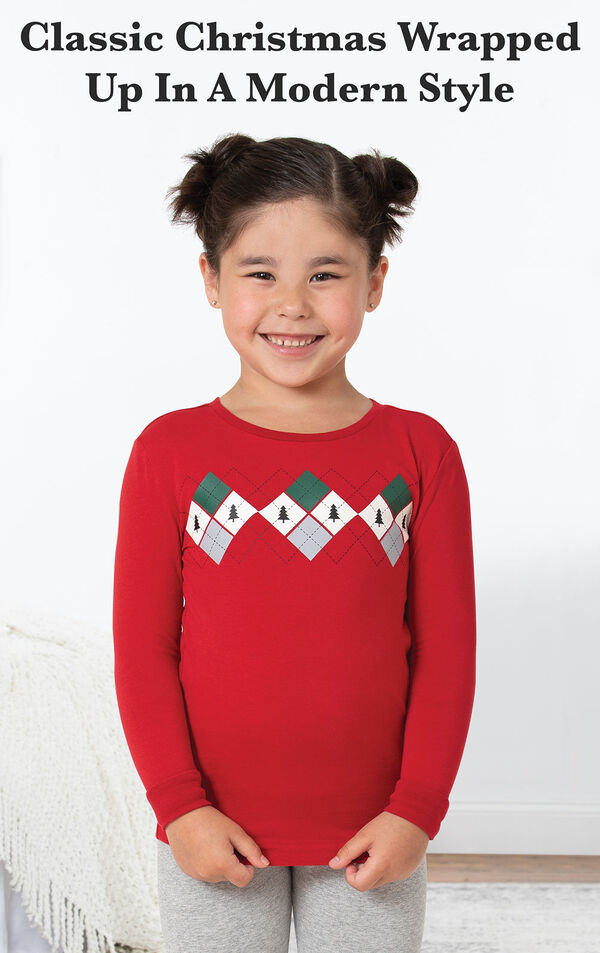 Model standing by bed wearing Red and Gray Holiday Argyle Girl's Pajamas with the following copy: Classic Christmas wrapped up in a modern style