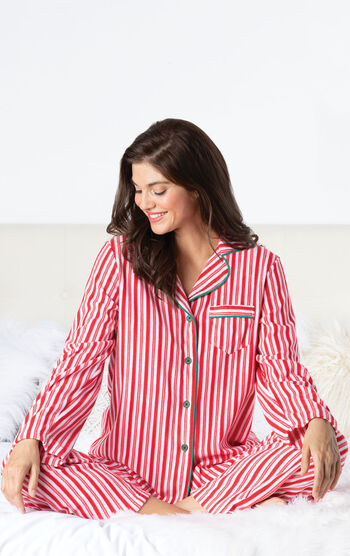 Model sitting on bed wearing Red and White Stripe Candy Cane Fleece Pajamas