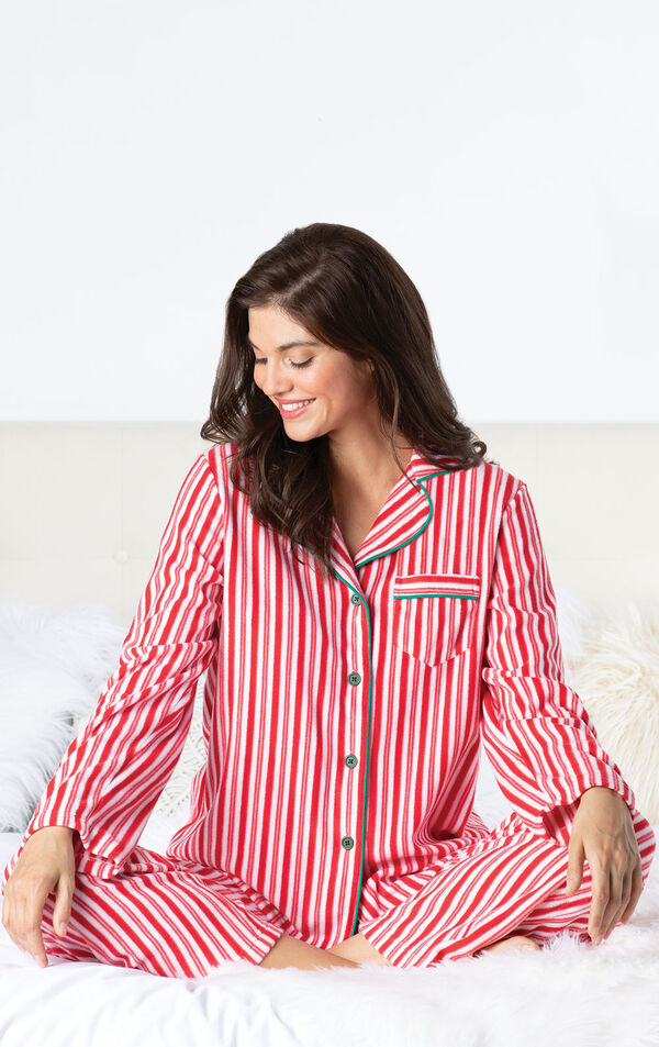 Model sitting on bed wearing Red and White Stripe Candy Cane Fleece Pajamas image number 1