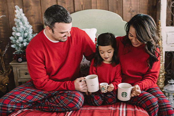 A family sitting on a bed wearing PajamaGram Stewart Plaid Flannel matching pajamas