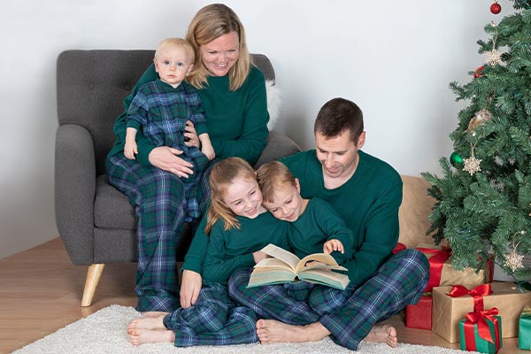 A young family and their children in front of a Christmas tree wearing matching PajamaGram Heritage Plaid pajamas