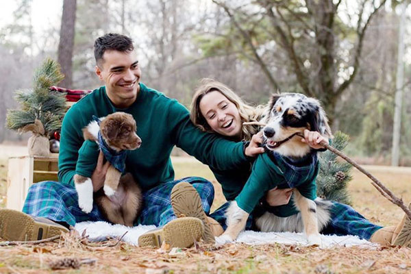 A Young couple and two dogs all wearing matching Heritage Plaid pajamas