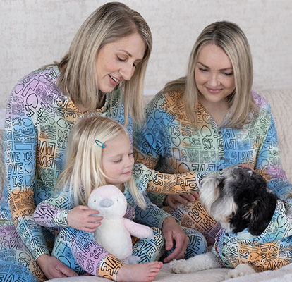 2 women, a young girl and a dog playing on a couch, all wearing Love is Love Couples Pajamas