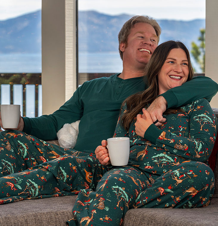 A young couple sitting on a couch enjoying coffee wearing Pajamagram Fun & Festive Matching Pajamas